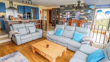 Ein modernes Wohnzimmer mit zwei grauen Sofas, einem Holztisch und einer Küche im Hintergrund.