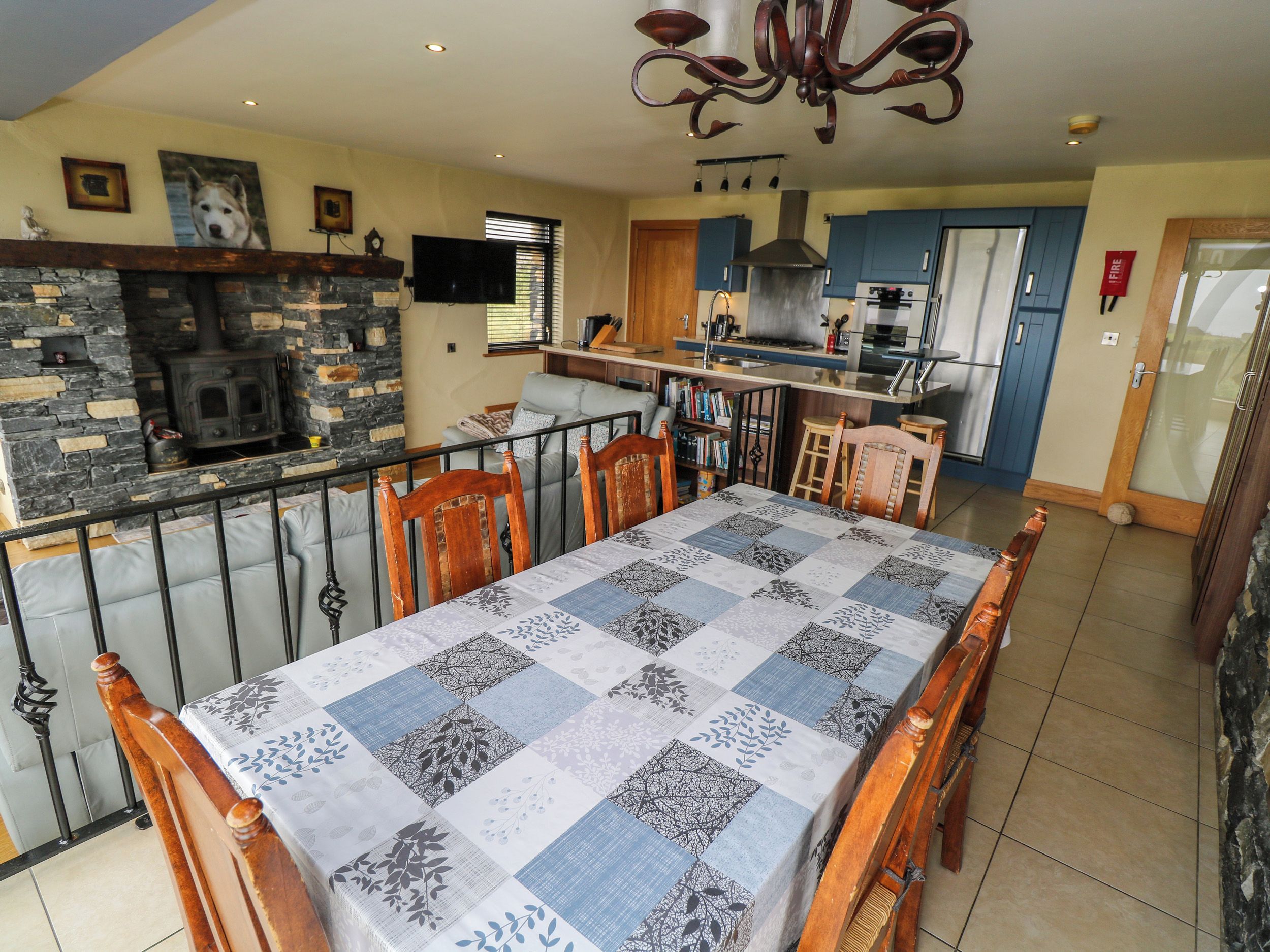 A dining area with a table set for four, a stone fireplace, and a kitchen in the background.