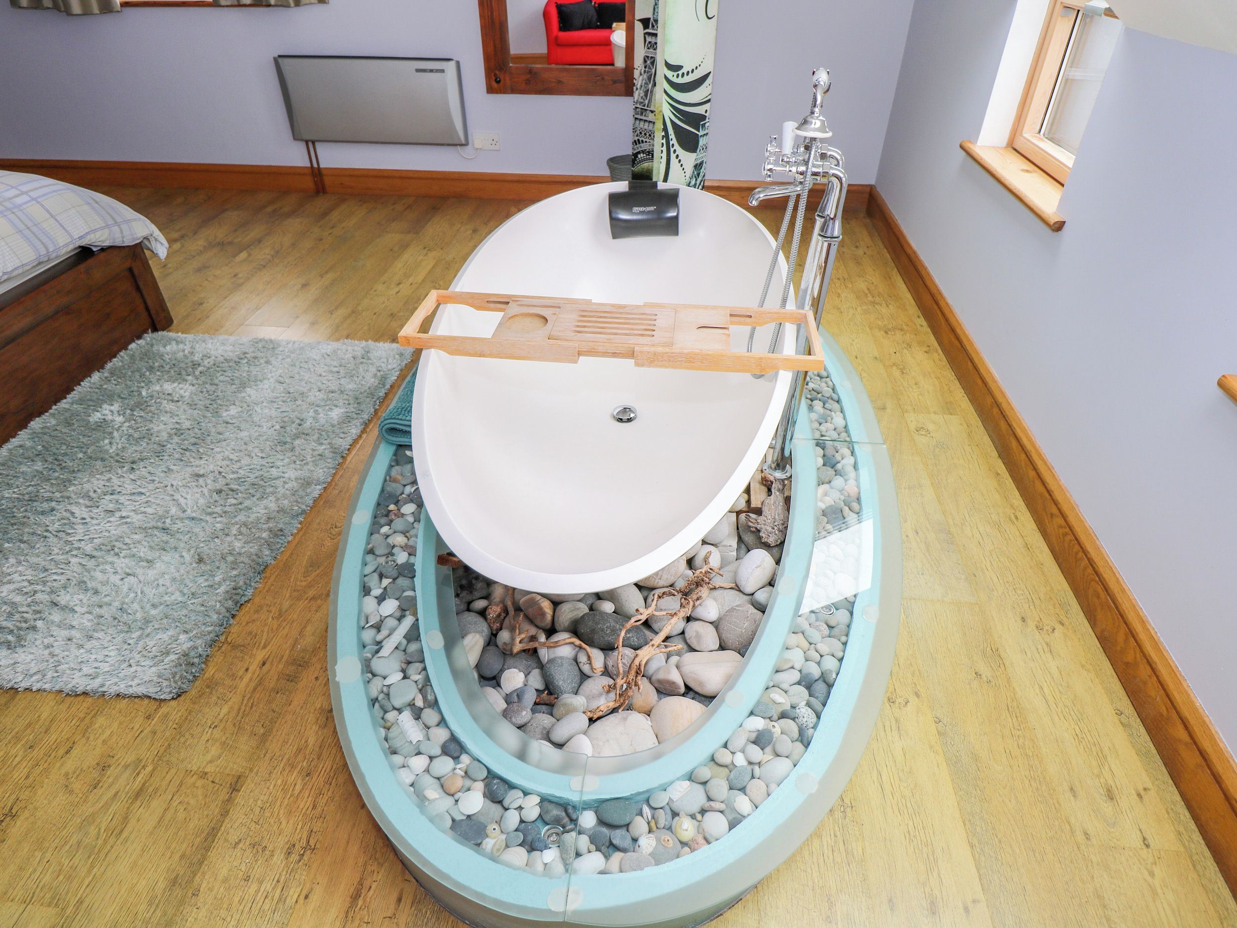 A bathroom with a freestanding bathtub, a wooden bath mat, and a small window.