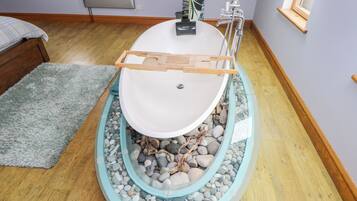 A bathroom with a freestanding bathtub, a wooden bath mat, and a small window.