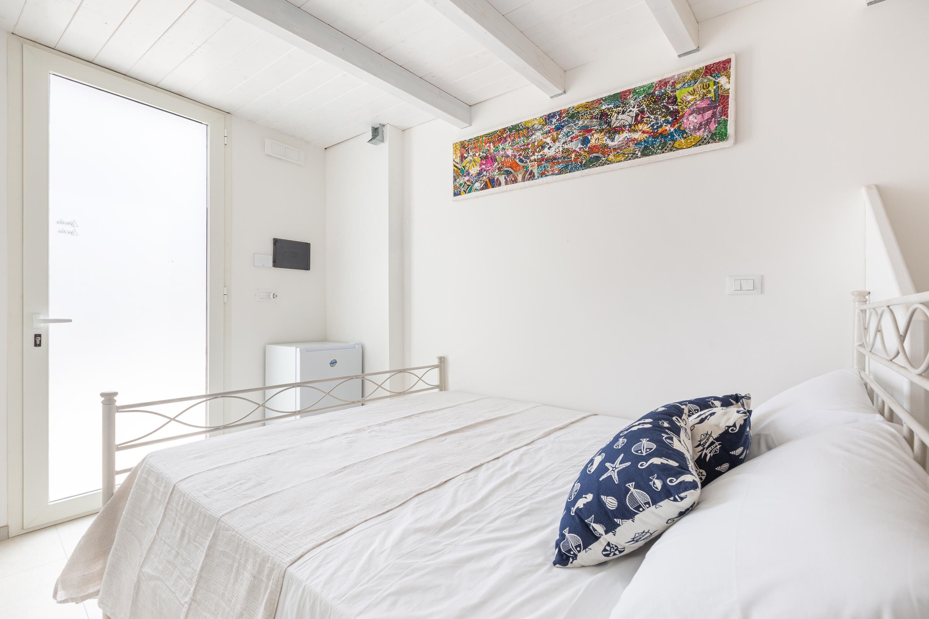 Quarto com cama, porta, obra de arte na parede e um pequeno armário.