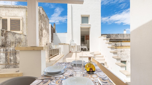 A balcony with a table set for dining, overlooking a white building with a window and a door. - 3471 Lecasinedico` - Linda Lucia by Barbarhouse (Castrignano del Capo)