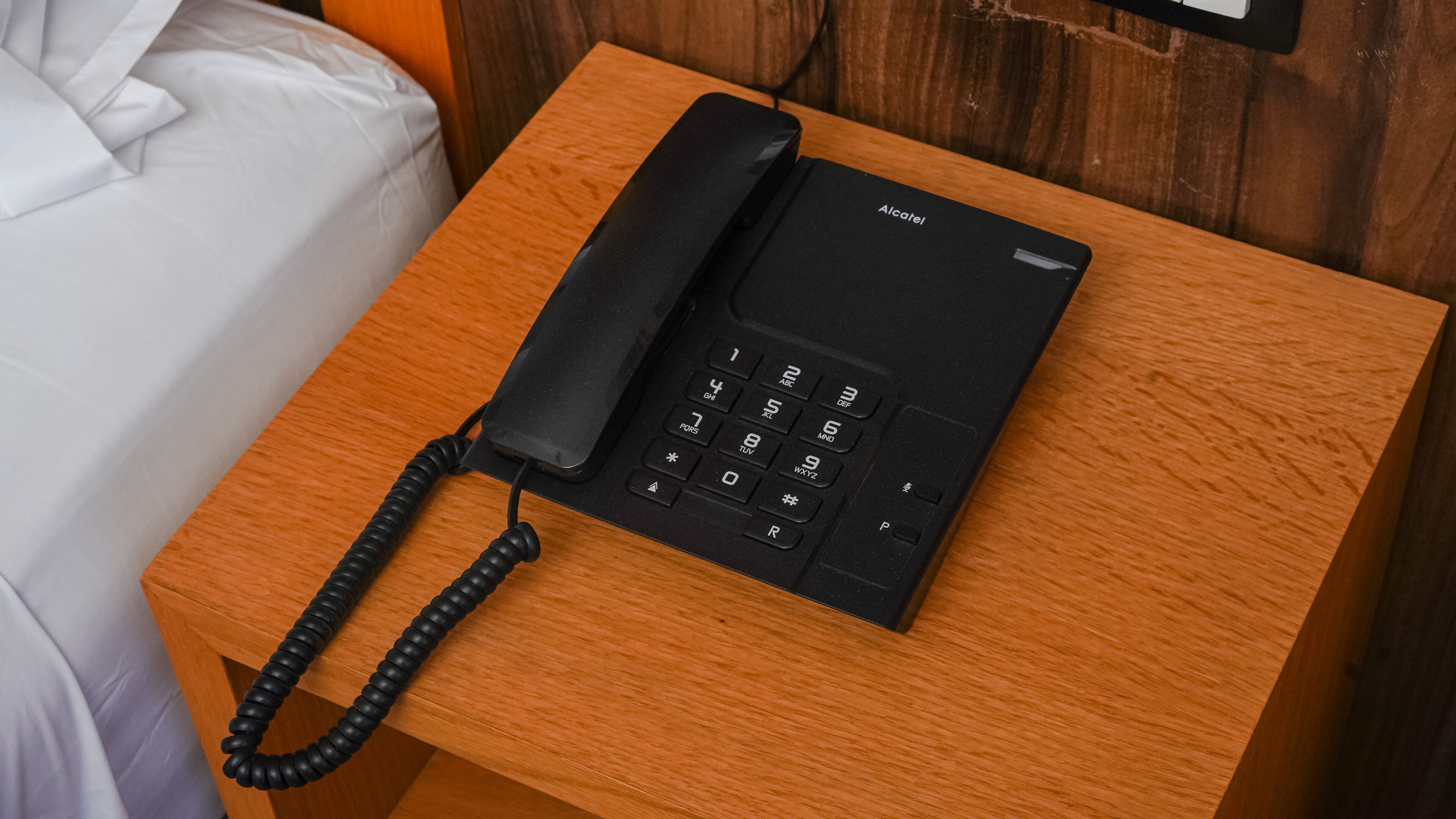 A black Alcatel phone on a wooden nightstand.