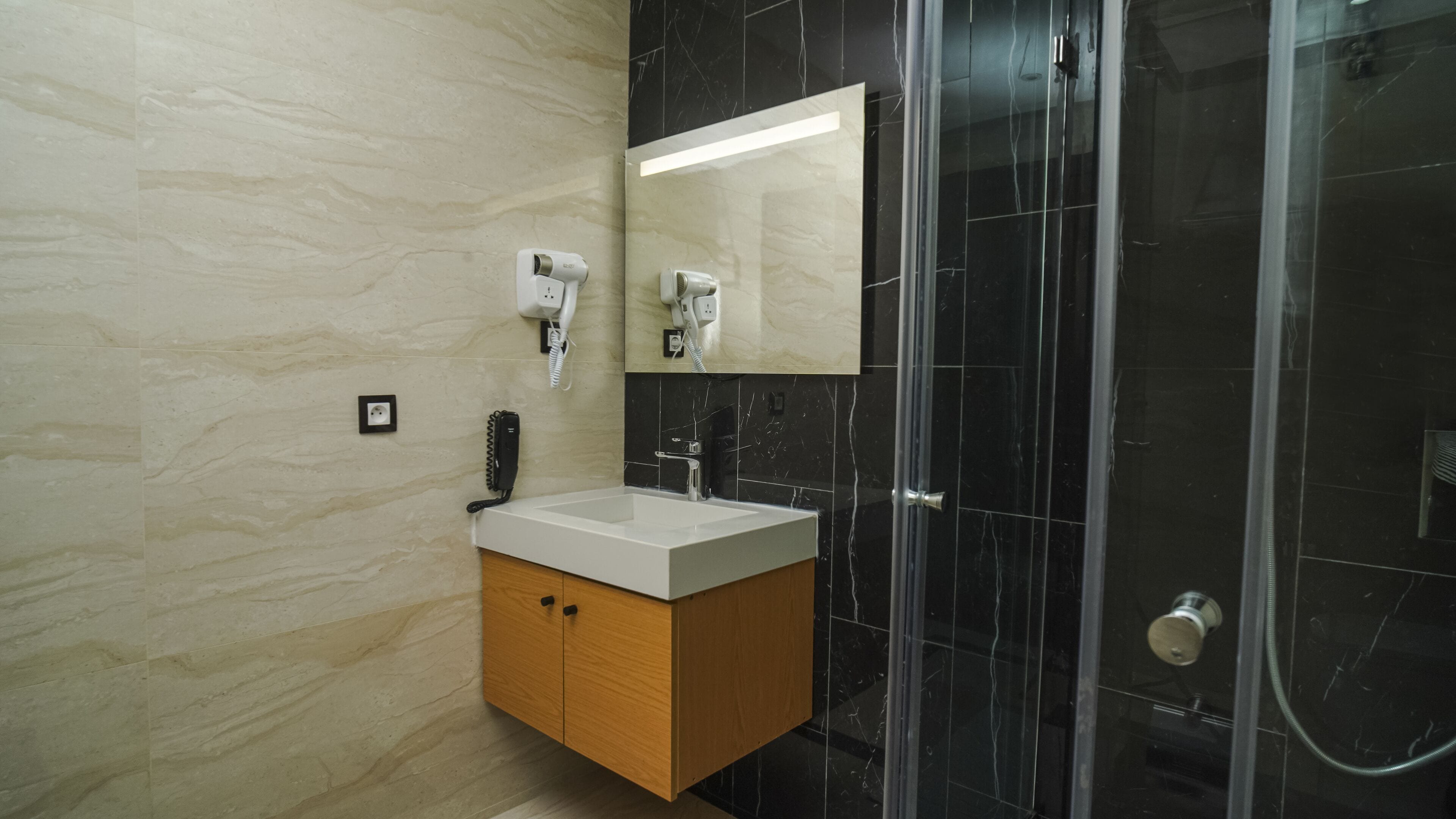 A modern bathroom with a marble vanity, a hairdryer, and a glass shower enclosure.
