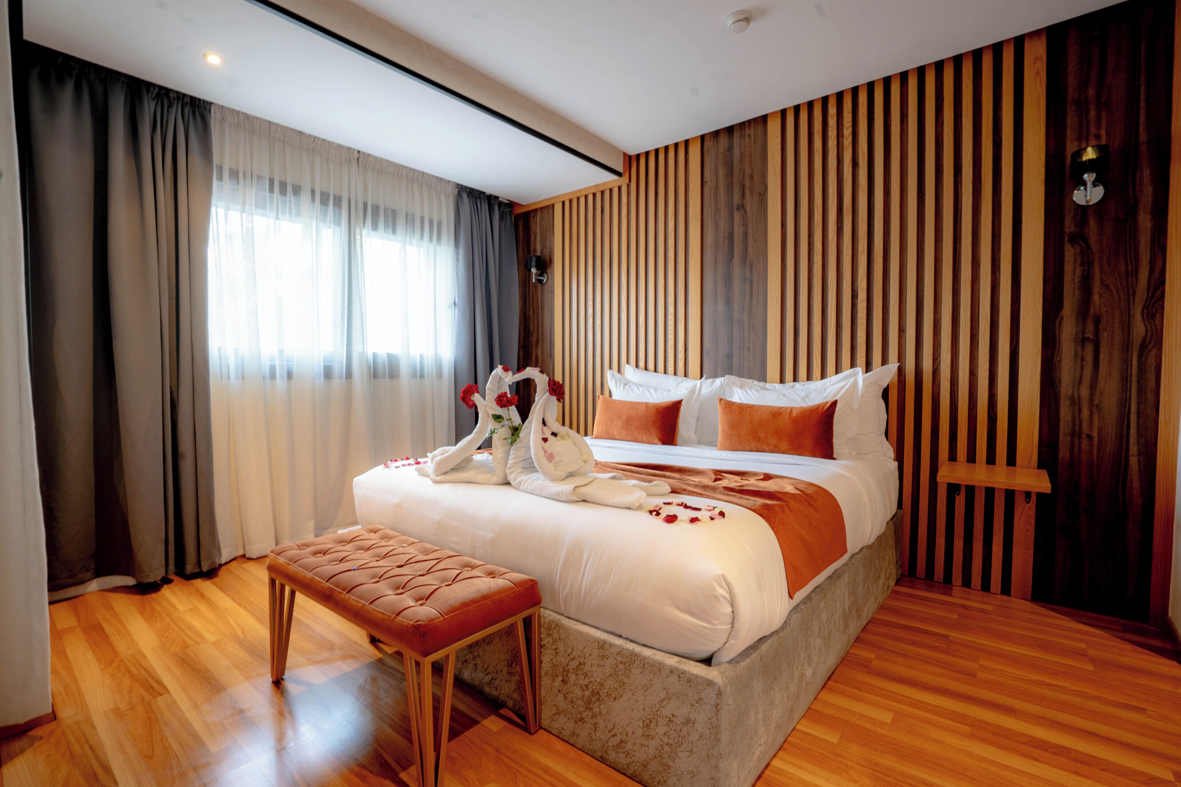 A modern bedroom with a large bed, wooden panel wall, and a bench.