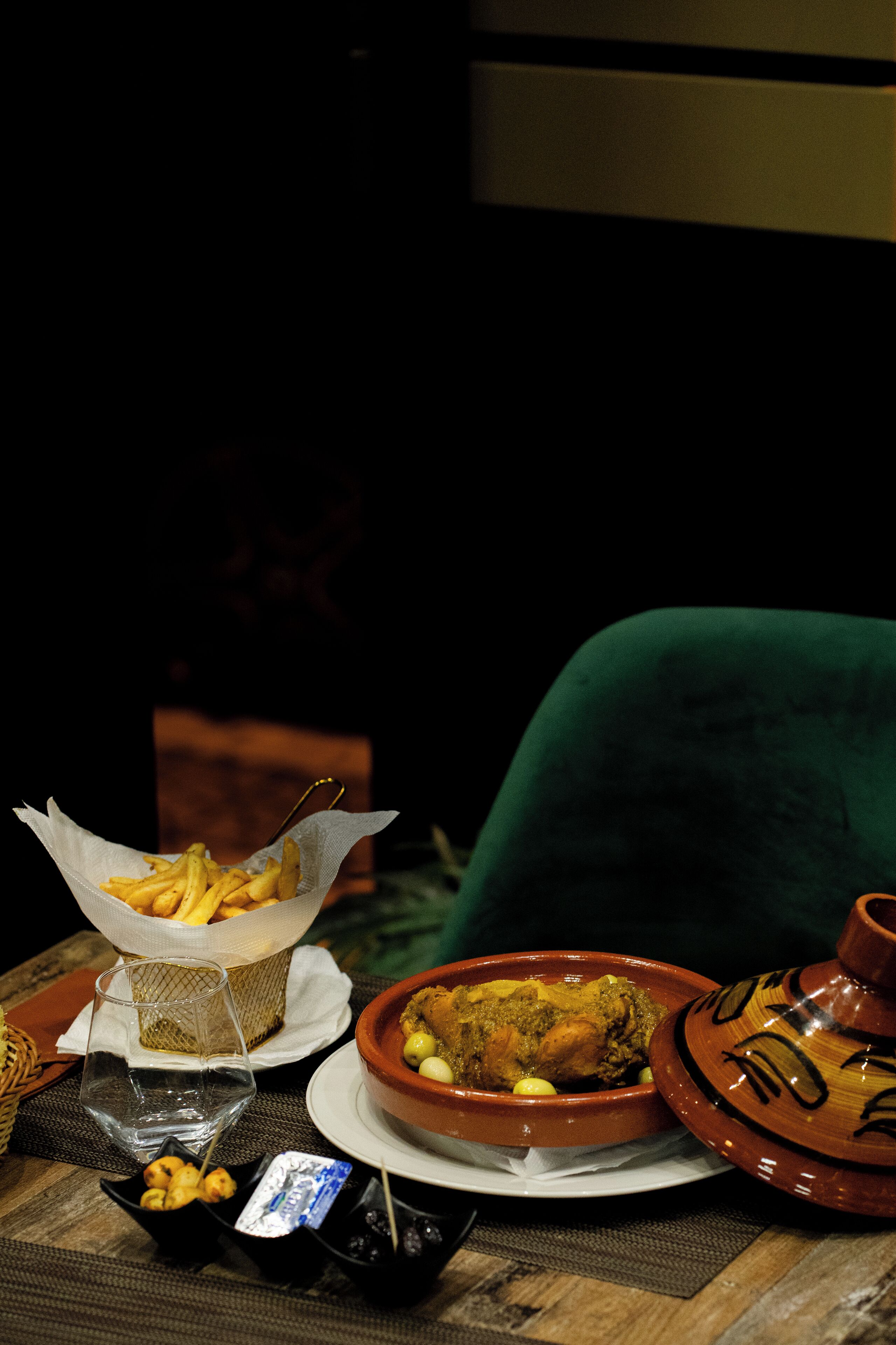 A table with a bowl of food, a basket of fries, a glass, and a ceramic pot.
