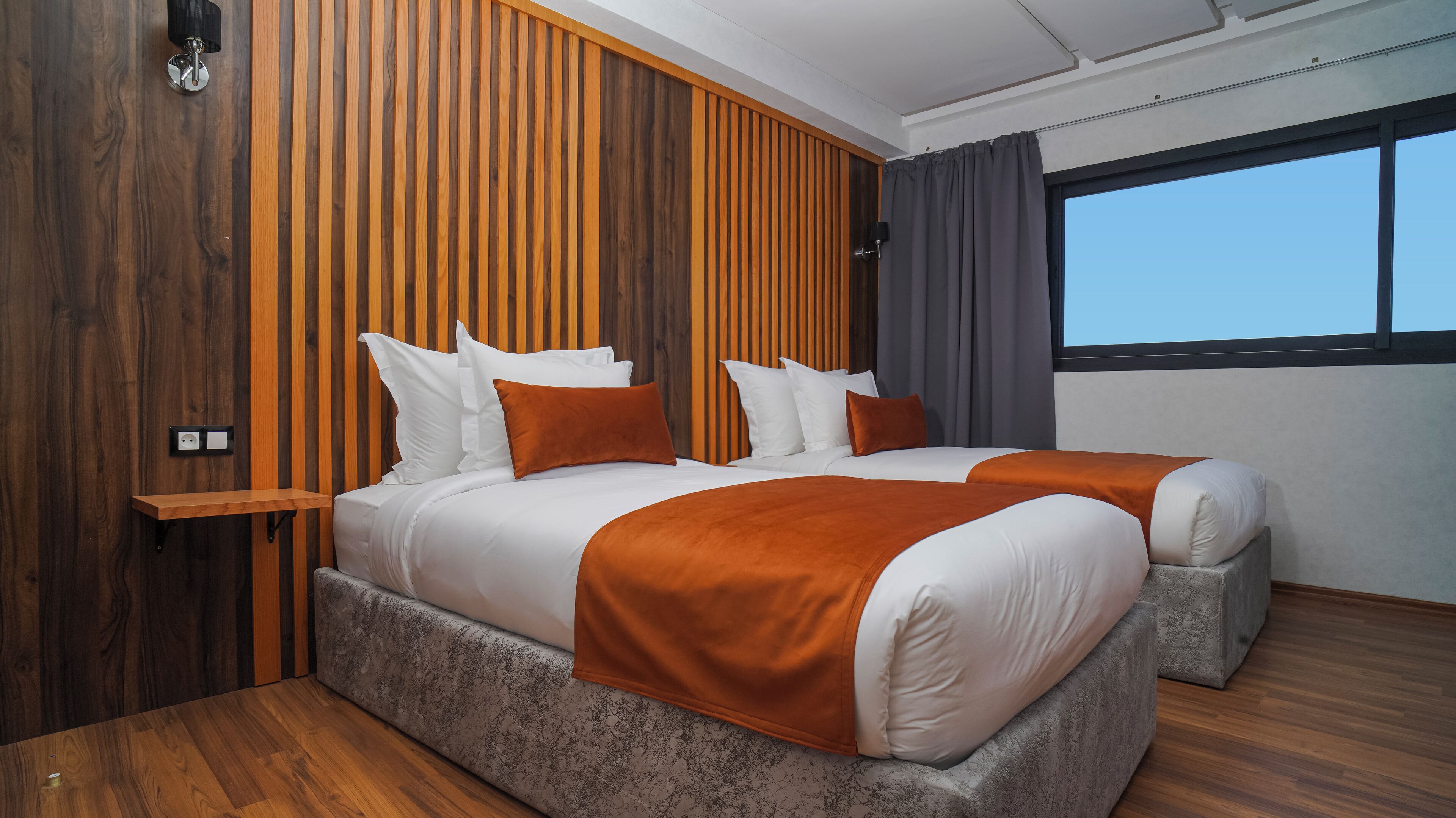 Ett modernt hotellrum med en stor säng, träpanel på väggarna, ett fönster med gardiner och ett trägolv.
