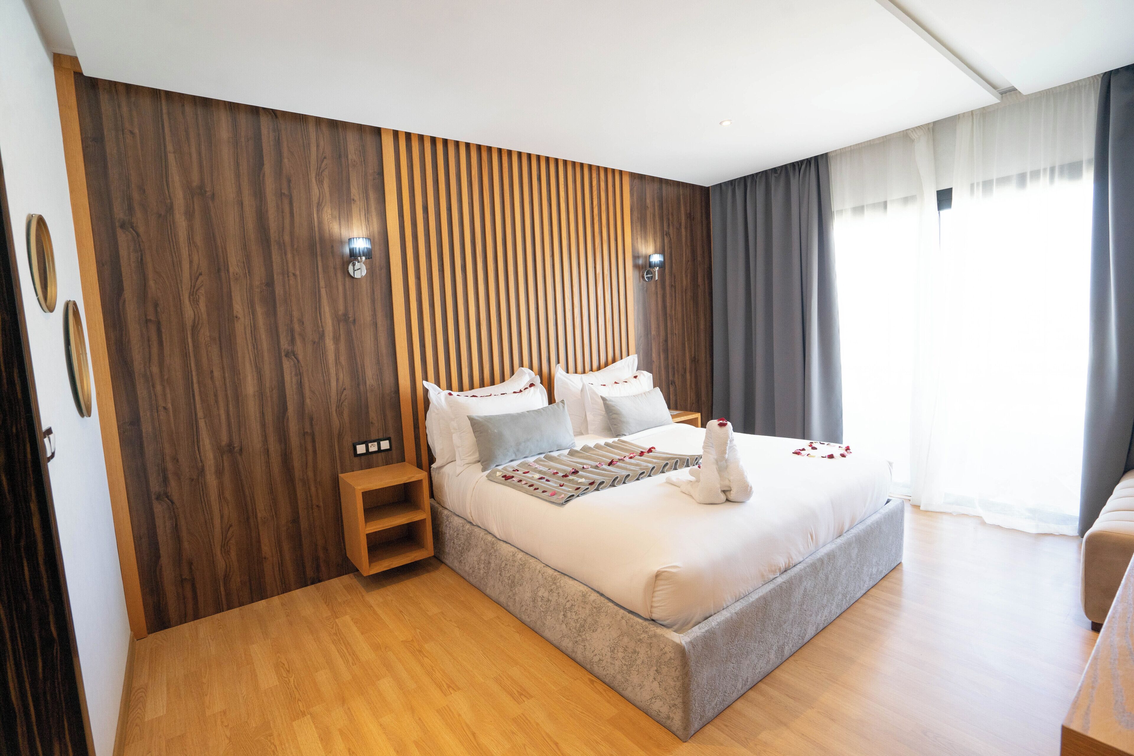 Un dormitorio moderno con una pared de acento de madera, una cama grande con cubrecama blanco, una mesita de noche y una lámpara de noche.