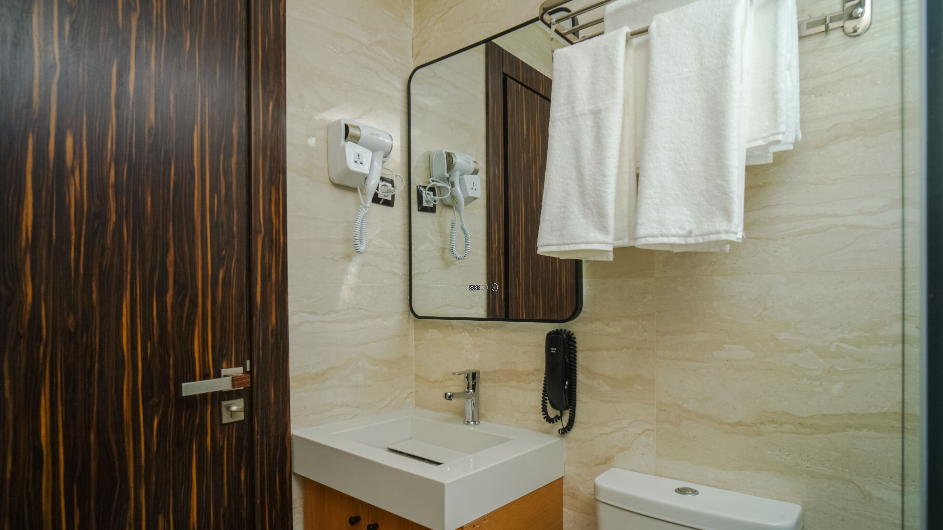 A bathroom with a wooden door, a white sink, a mirror, a hairdryer, and a toilet.