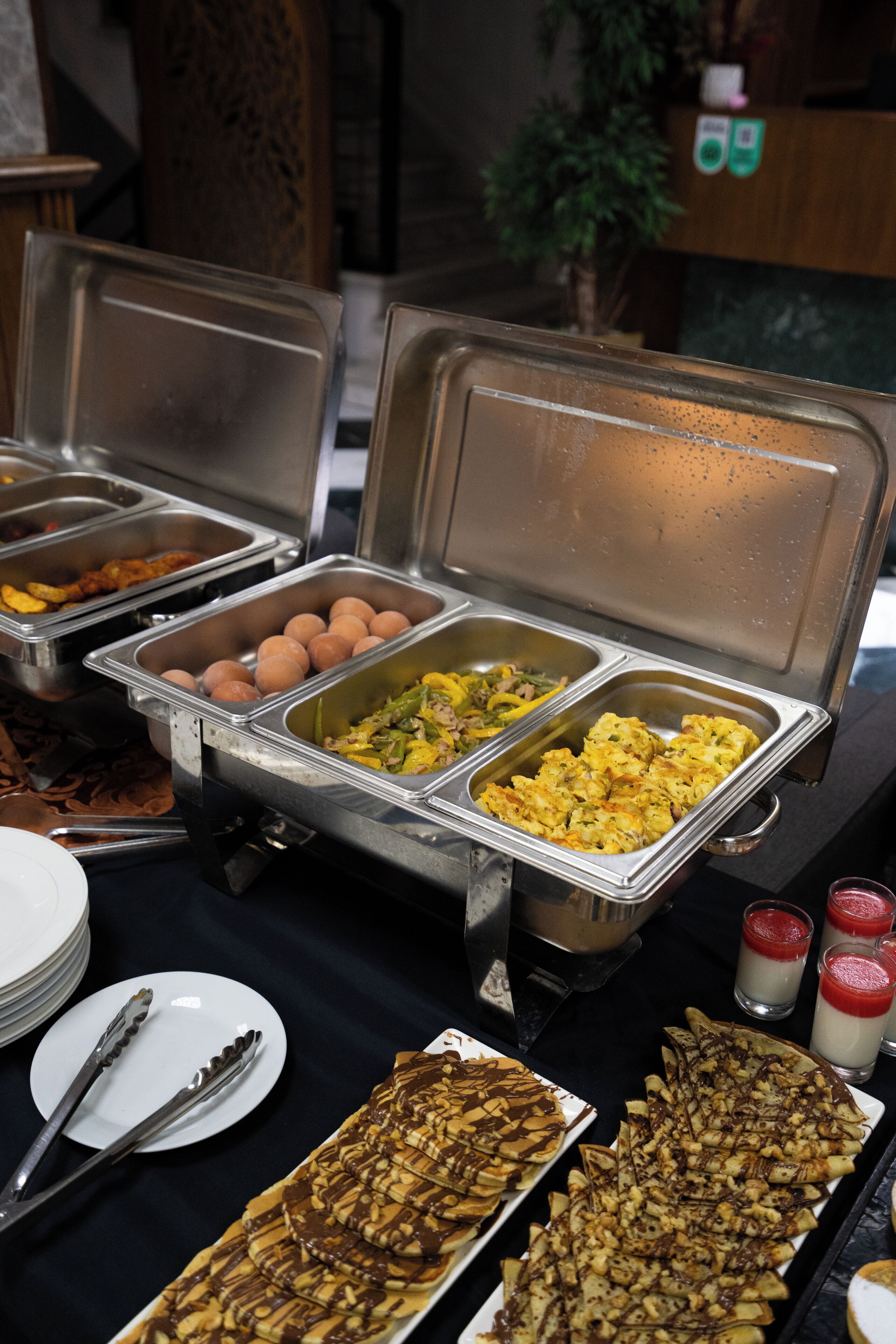 Un buffet proposant une variété de plats, notamment des œufs, des légumes et des crêpes.