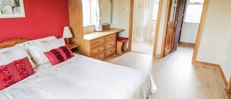 A bedroom with a large bed, a wooden dresser, a mirror, and a door leading to another room.