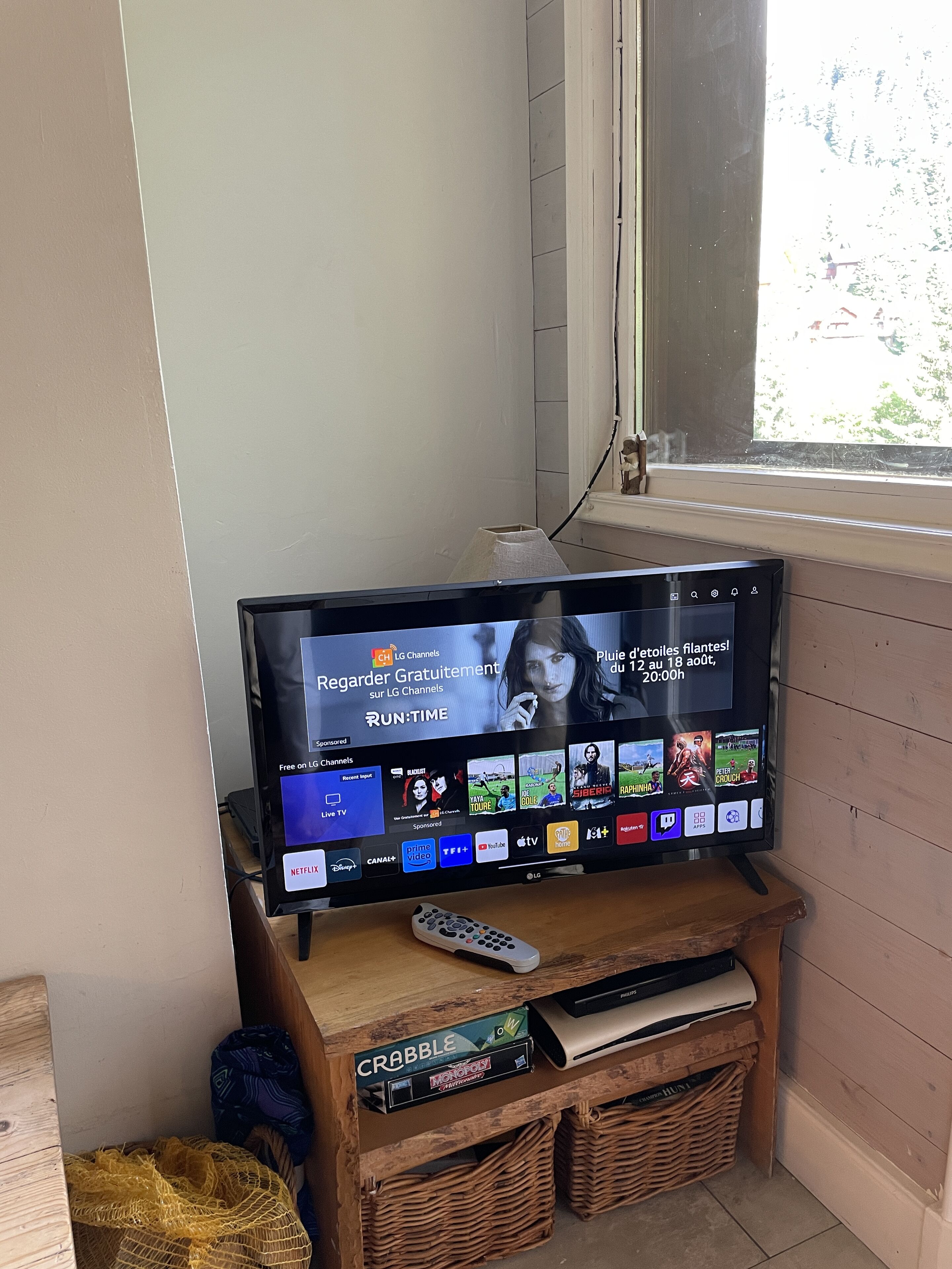 Televisor sobre un suport de fusta amb un comandament a distància, una cistella i una petita prestatgeria amb llibres.