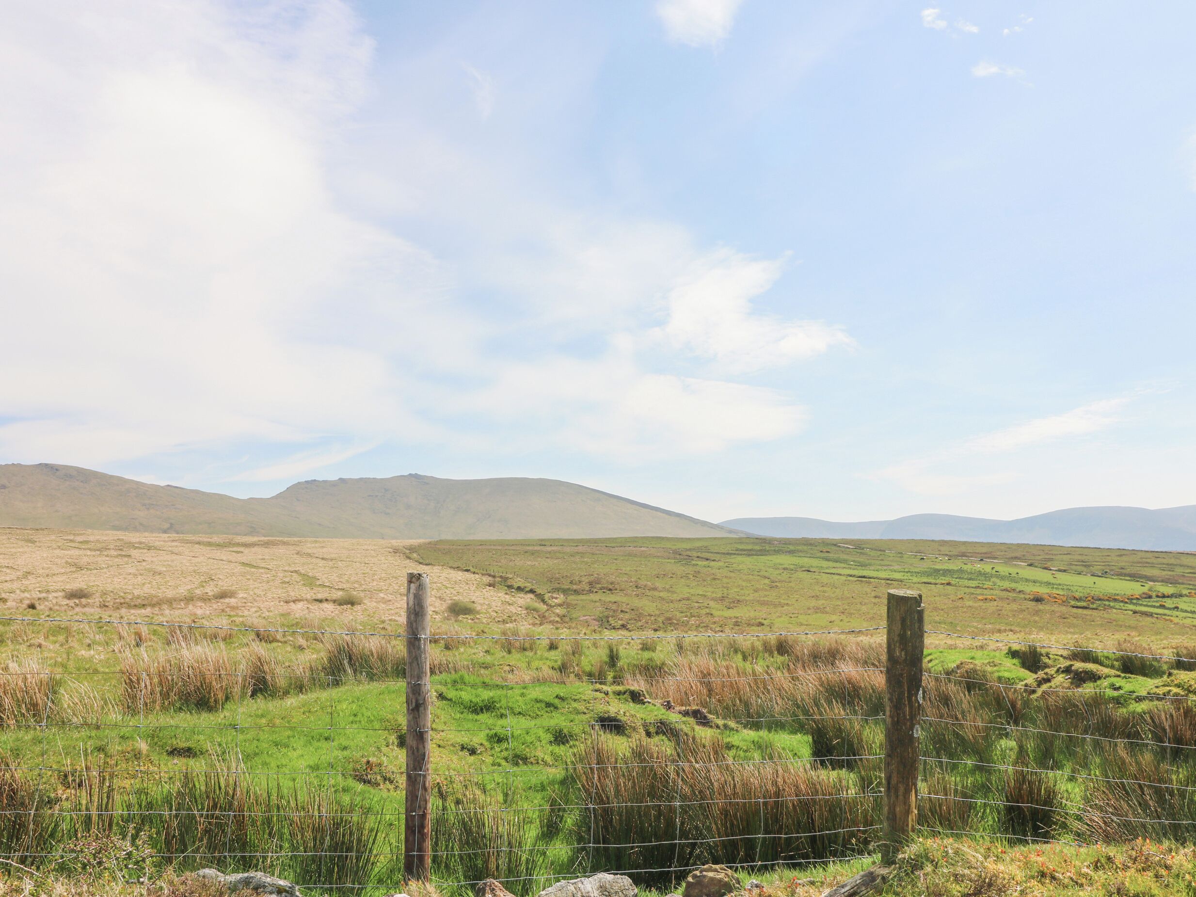 A rural landscape with a grassy field, a wooden fence, and distant hills.