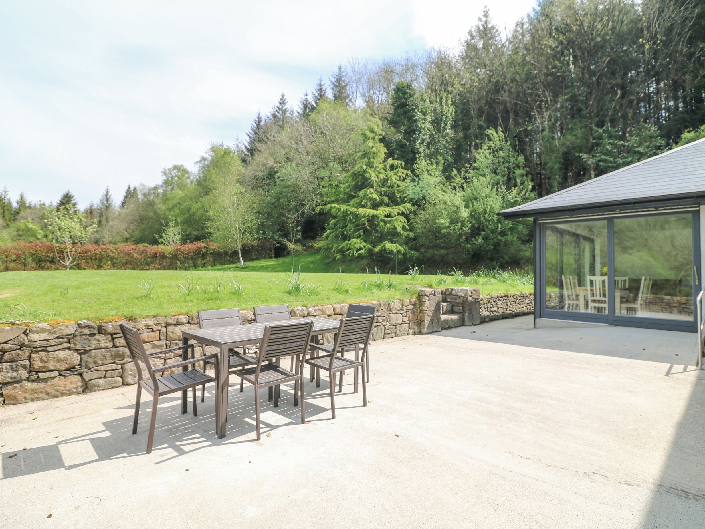 An outdoor patio with a stone wall, a table with chairs, and a glass-enclosed area.