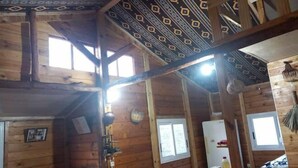 Interior de una cabaña de madera con techo alto, diseño de techo con motivos y estructura central de viga de madera.