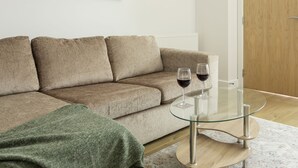 A beige sofa with a glass coffee table and two wine glasses. - 1 Bedroom Luxury Apartment in Redhill (Redhill)