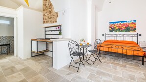 A compact room with a bed, a desk, and a chair. There is a painting on the wall and a potted plant on the desk. - 3396 Leucadense - Grotta 1 by Barbarhouse (Castrignano del Capo)