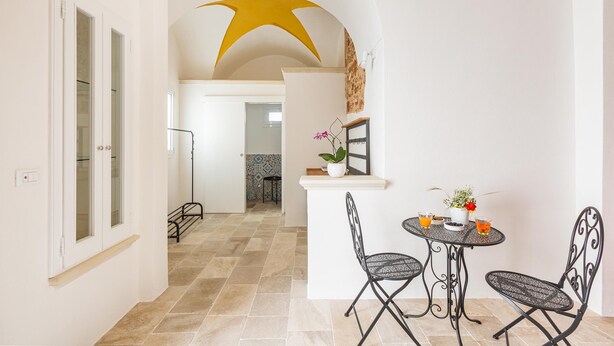 A dining area with a round table and two chairs, a small white counter with a plant, and a yellow star-shaped ceiling design. - 3396 Leucadense - Grotta 1 by Barbarhouse (Castrignano del Capo)