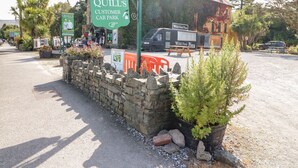 Un mur de pierre avec une pancarte indiquant le parking réservé aux clients de Quill, un camion-restaurant et un bâtiment avec un toit en tuiles.