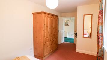 Un dormitorio con un armario de madera, una cama con manta a rayas, un espejo y una puerta que da a otra habitación.