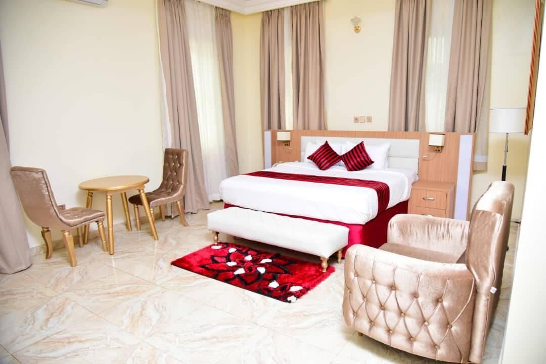 Quarto de hotel com cama, mesas de cabeceira, uma cadeira, uma pequena mesa e um tapete floral vermelho.