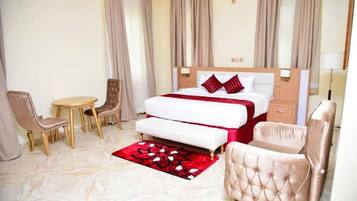 Quarto de hotel com cama, mesas de cabeceira, uma cadeira, uma pequena mesa e um tapete floral vermelho.