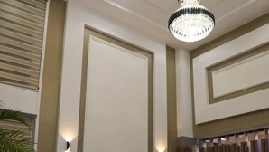 Eine Lobby mit hohen Decken, einer Kristalllüster, Wandleuchten und Sitzbereichen.