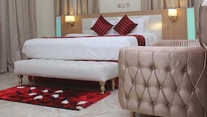 Ein Hotelzimmer mit einem großen Bett, zwei Nachttischlampen, einem roten und weißen Teppich sowie einem gepolsterten Ohrensessel.