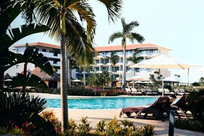 A pool area with lounge chairs, palm trees, and a building with multiple balconies in the background. - Elegant Hotel & Suites by City Green   (Jimeta)