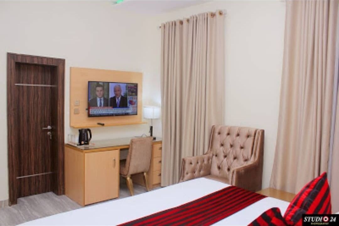 A hotel room with a bed, a desk, a chair, a television, and curtains.