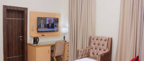 Una habitación de hotel con cama, escritorio, silla, televisor y cortinas.