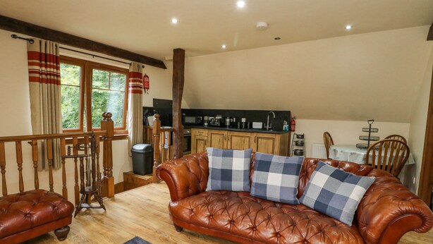 A cozy living room with a leather sofa, wooden flooring, and a kitchen area in the background. - Glenmhor Apartment (Fort William)