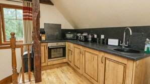 A kitchen with wooden cabinets, a black countertop, a stainless steel sink, and a window with curtains. - Glenmhor Apartment (Fort William)