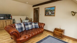 A cozy living room with a leather sofa, a dining table with chairs, a kitchen area, and a painting on the wall. - Glenmhor Apartment (Fort William)