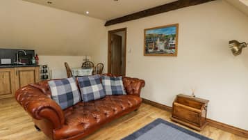 A cozy living room with a leather sofa, a dining table with chairs, a kitchen area, and a painting on the wall.