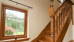 A wooden staircase with a handrail and a window with a view of a garden. - Glenmhor Apartment (Fort William)