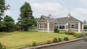 A two-story house with a brick exterior and white trim, a covered porch, and a well-maintained lawn. - CHURCHFIELD HOUSE, pet friendly in Crossmolina, County Mayo (Ballina)
