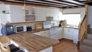 A kitchen with white cabinets, a wooden countertop, a stove, a microwave, and a sink.