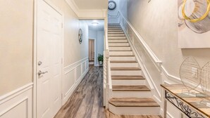 A hallway with a wooden staircase, white walls, and a clock on the wall. - 3BR Townhouse Right in Front of Epic Universe! (Orlando)
