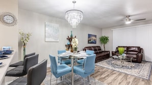 A modern living room with a dining area, featuring a chandelier, leather sofas, and a large rug. - 3BR Townhouse Right in Front of Epic Universe! (Orlando)