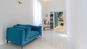 A modern living room with a blue sofa, a pendant light, and a view into an adjacent room with a painting.