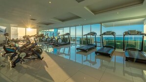 Ein modernes Fitnessstudio mit verschiedenen Trainingsgeräten, großen Fenstern und Blick auf den Ozean.