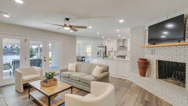 A modern living room with a sofa, coffee table, and chairs, a fireplace, and a television mounted on a brick wall. - Waterfront Hot Springs Home w/ Dock & Porch! (Hot Springs)