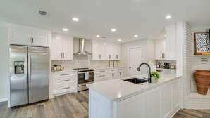 A modern kitchen with white cabinetry, a stainless steel refrigerator, an island with a sink, and a built-in stove. - Waterfront Hot Springs Home w/ Dock & Porch! (Hot Springs)