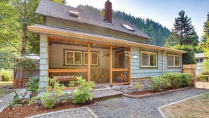 A two-story house with a covered porch, stone foundation, and a gravel driveway. - Historic Mapleton Cottage w/ River Views & Hot Tub (Mapleton)