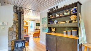 A cozy living room with a stone wall, a fireplace, a cabinet with decorative items, and a 'DREAM' sign on the wall. - Historic Mapleton Cottage w/ River Views & Hot Tub (Mapleton)