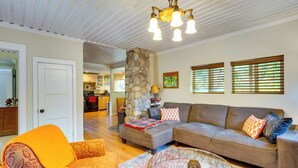 A spacious living room with a sofa, armchair, and ottoman, a dining area in the background, and a kitchen visible through an open door. - Historic Mapleton Cottage w/ River Views & Hot Tub (Mapleton)