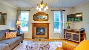 A living room with a fireplace, a sofa, a coffee table, and a television. - Historic Mapleton Cottage w/ River Views & Hot Tub (Mapleton)