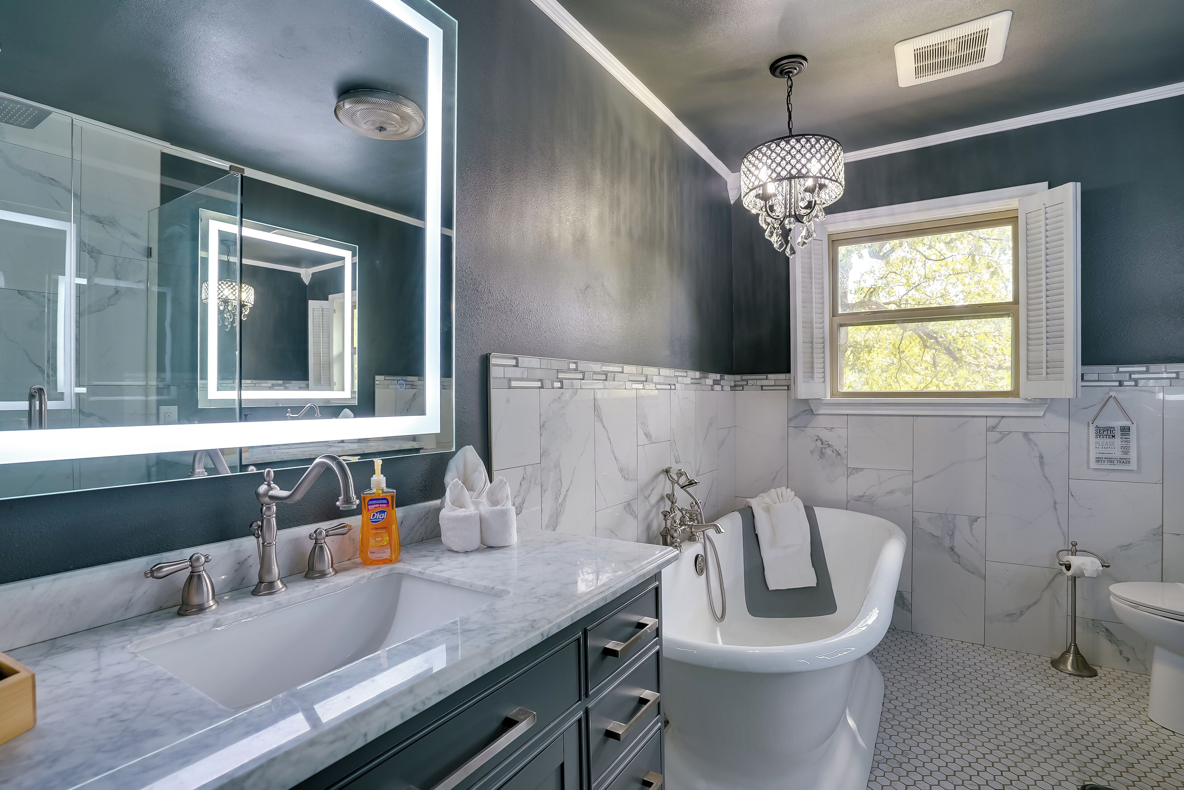 A modern bathroom with a large mirror, a white bathtub, and a sink with a marble countertop.