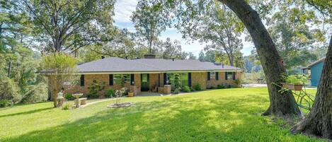 A single-story house with a sloped roof, surrounded by a well-maintained lawn and large trees.